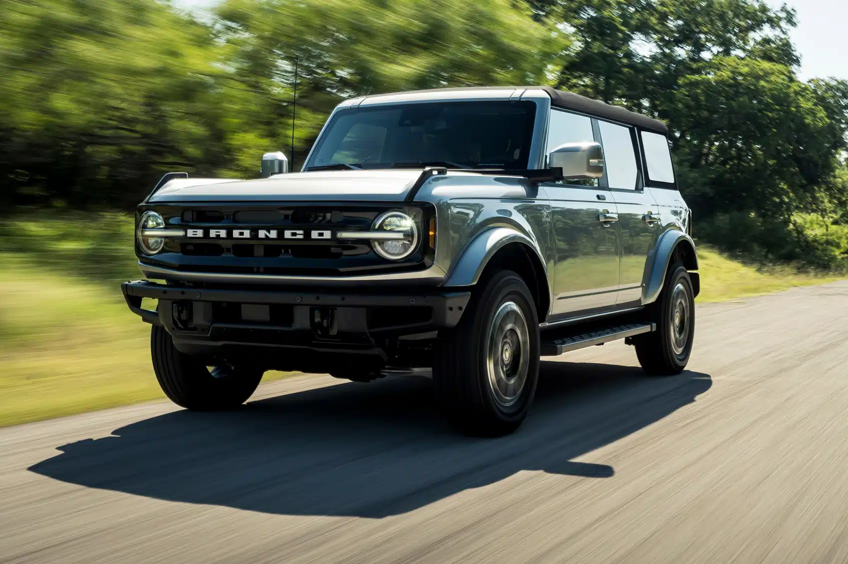 Modern Ford Bronco driving on a scenic road, showcasing its rugged design and off-road capabilities with a vibrant green backdrop.