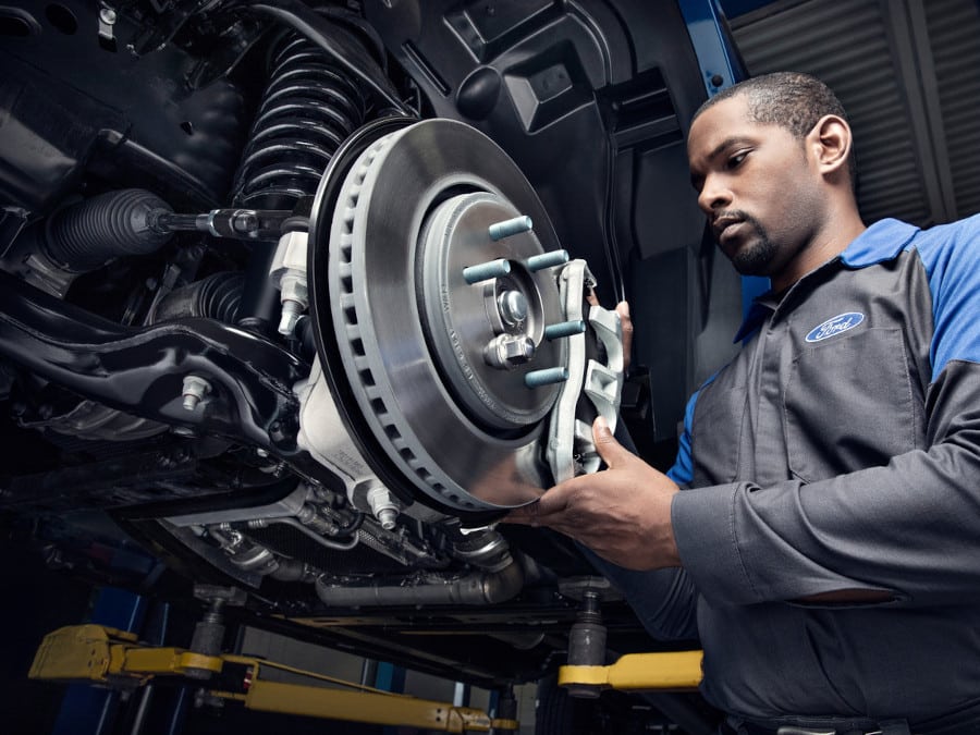 Automotive technician working on a vehicle's brake system, inspecting and handling brake components, with a focus on precision and safety in a professional garage setting.