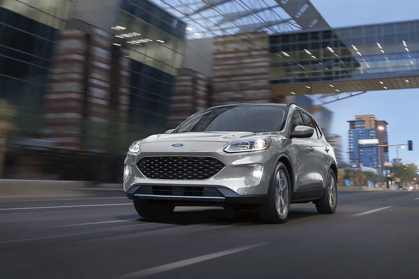 Silver Ford SUV driving through an urban setting at dusk, showcasing a modern design and dynamic performance.