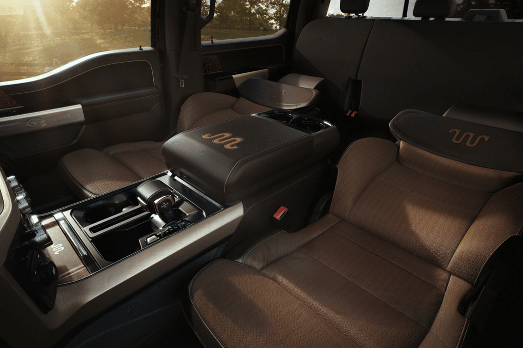 Interior view of a luxury truck showcasing plush brown seating with leather accents and a central console featuring a gear shift and storage compartments, illuminated by natural light. Ideal for advertisements highlighting comfort and style in modern vehicle interiors.