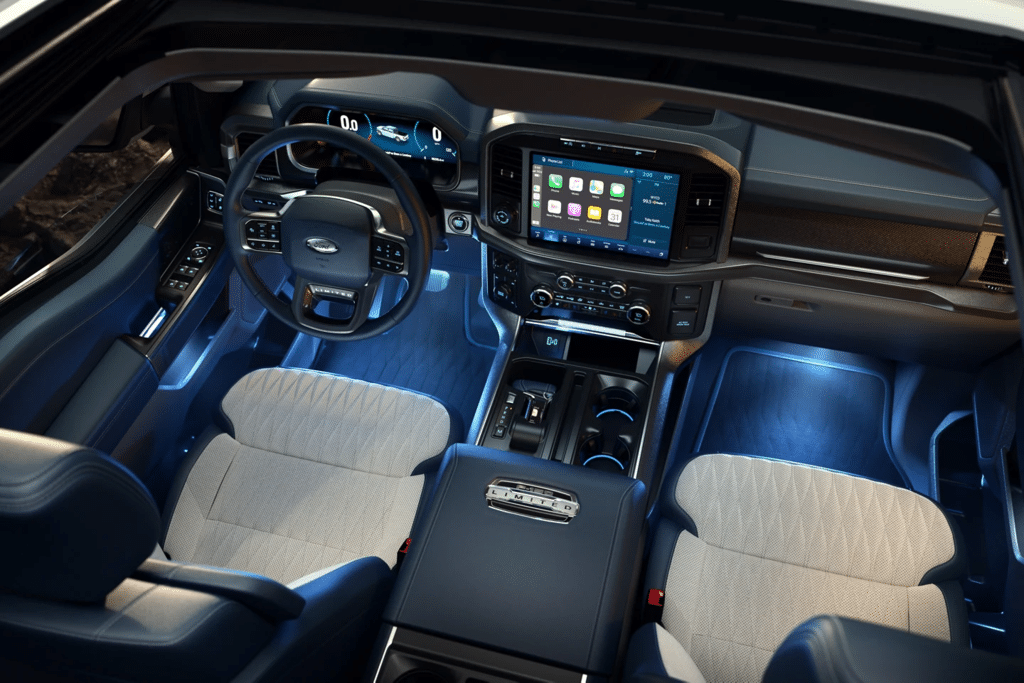 Interior view of a modern vehicle showcasing a sleek dashboard with digital display, advanced infotainment system, illuminated floor, and comfortable seating arrangement. The steering wheel and dashboard controls highlight user-friendly features and innovative design.