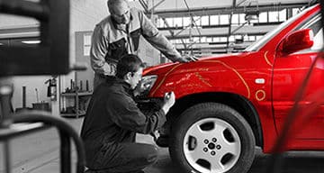 A technician in protective clothing spray paints a car inside a professional paint booth, with the vehicle covered in plastic to protect its surfaces.