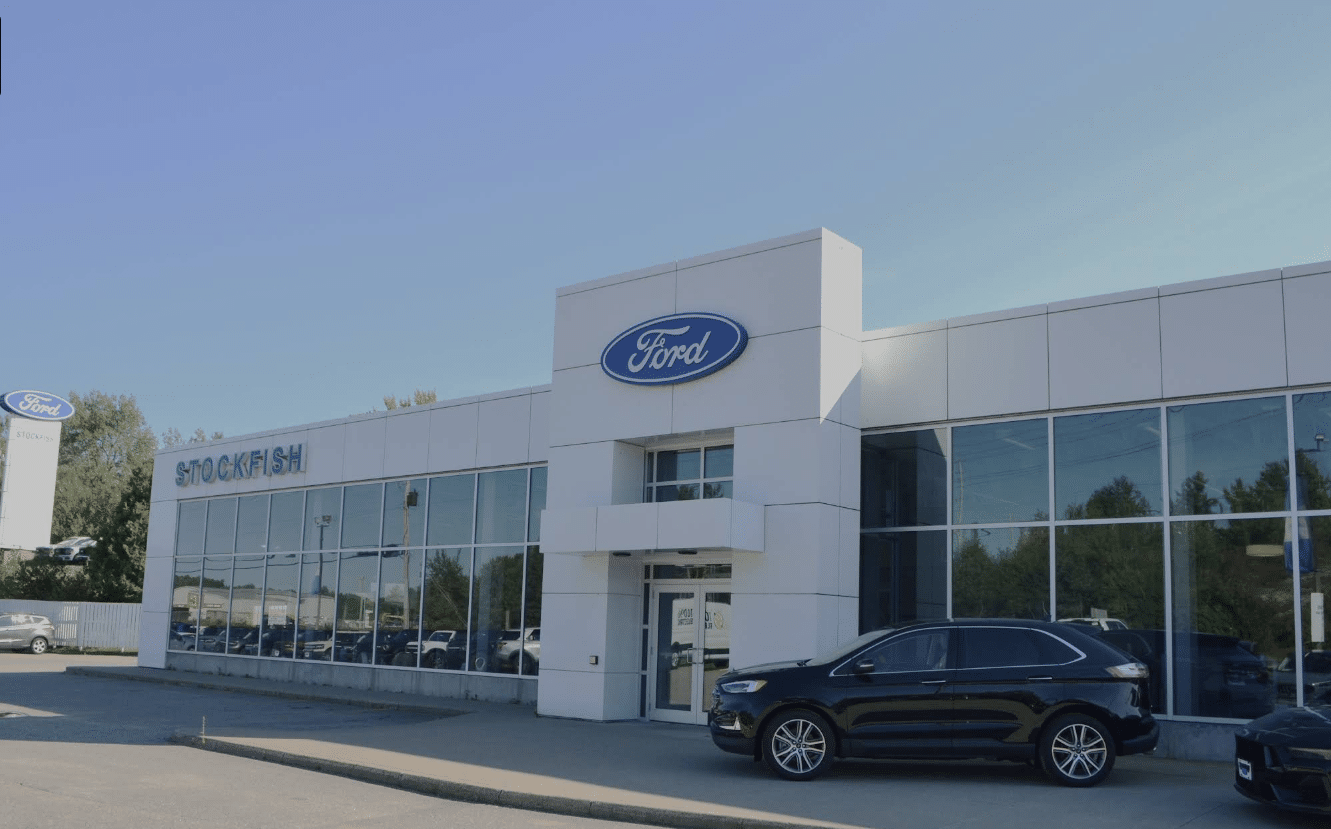 Ford dealership exterior with the Stockfish name prominently displayed, featuring a modern architectural design and a lineup of vehicles parked outside. Clear blue sky enhances the professional appearance of the location.